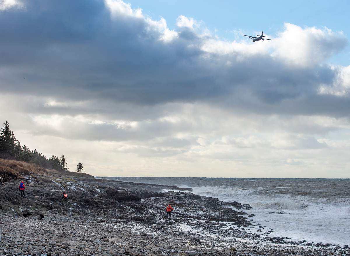 An RCAF Hercules aircraft scours the waters as members of a ground search and rescue team walk along the shore of the Bay of Fundy in Hillsburn, N.S., in an area where empty life-rafts from a scallop fishing vessel where reported on Tuesday, Dec. 15, 2020.