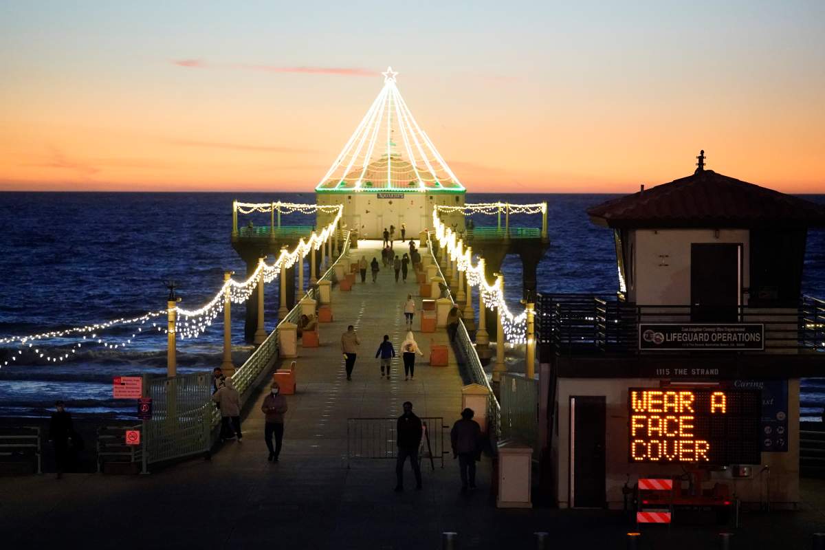 FILE - In this Dec. 14, 2020, file photo, a sign encourages visitors to wear a face cover amid the coronavirus pandemic on the pier in the Manhattan Beach section of Los Angeles.