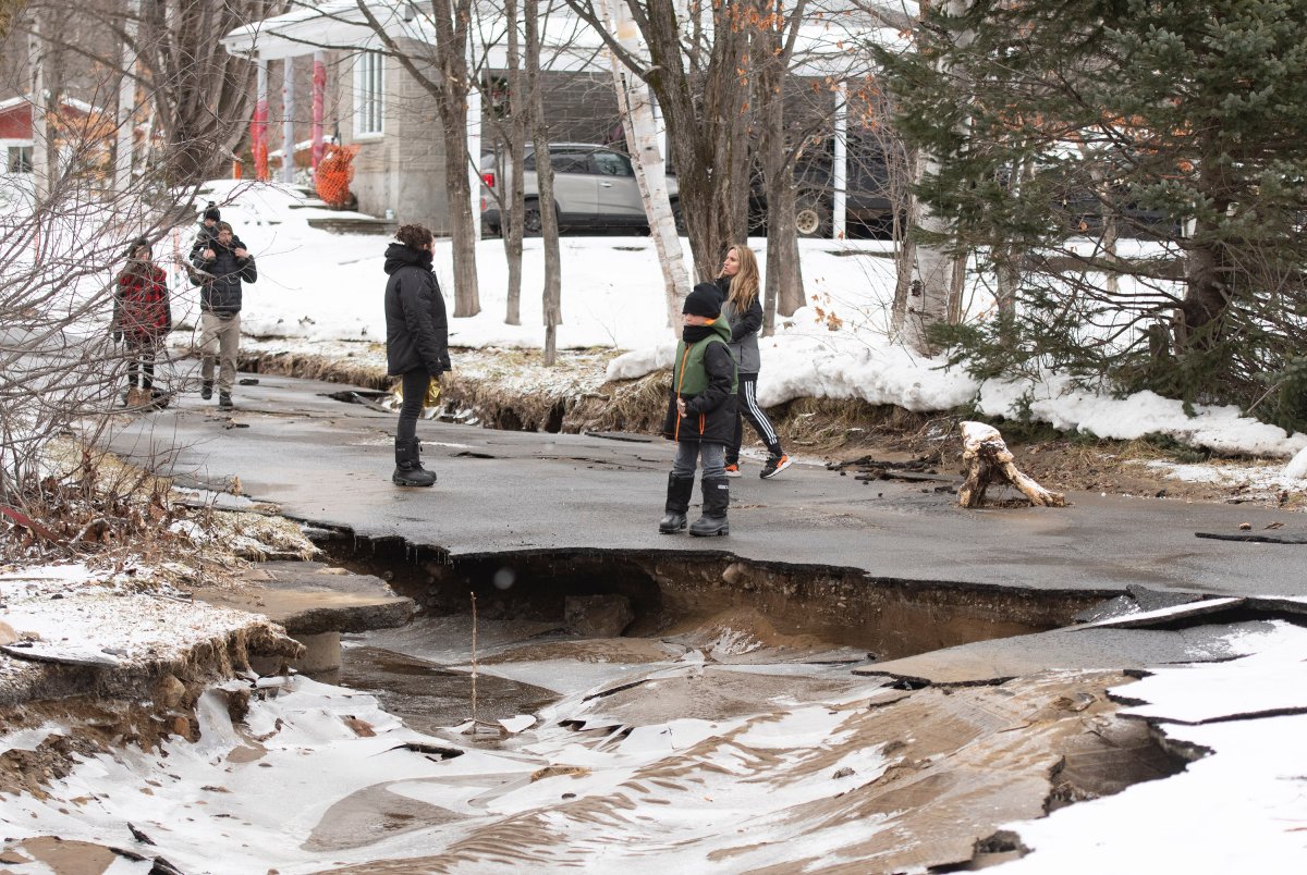 Stand on the remains of a washed-out street, in Sainte-Brigitte-de-Laval, Que., Saturday, Dec. 26, 2020. A flash flood forced the evacuation of residents on Christmas day, Dec. 25, as the waters of the Montmorency river came up because of heavy rains. 