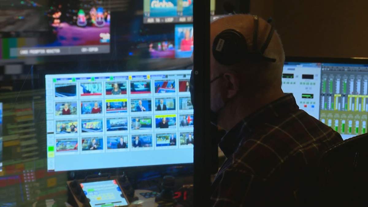 A Global News employee wearing a face mask sits behind a plastic barrier in the Global Calgary newsroom.