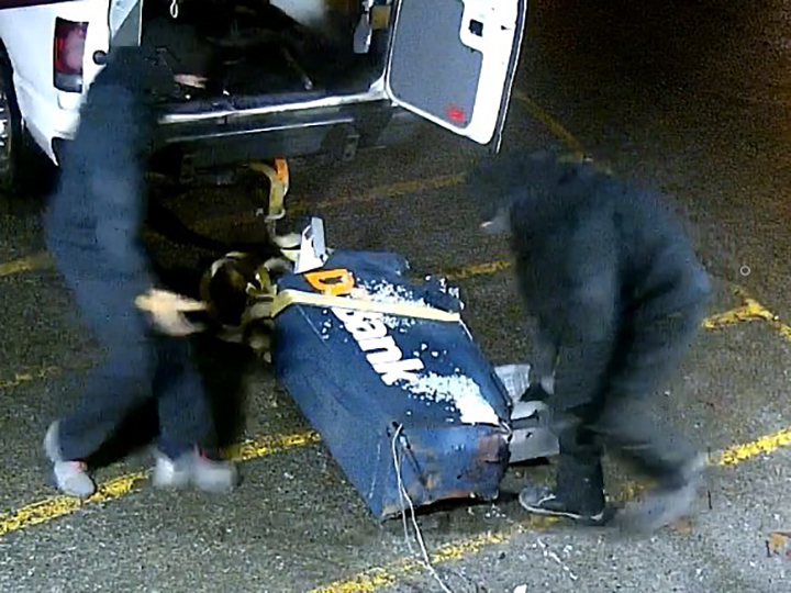 A screenshot from video survelliance showing two men loading the stolen ATM into the back of a white van.