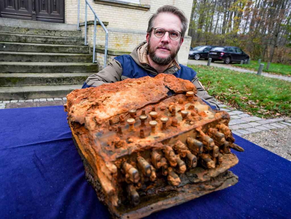 Florian Huber, research diver, kneels in front of the archaeological office of Schleswig-Holstein when handing over the Enigma cipher machine.
