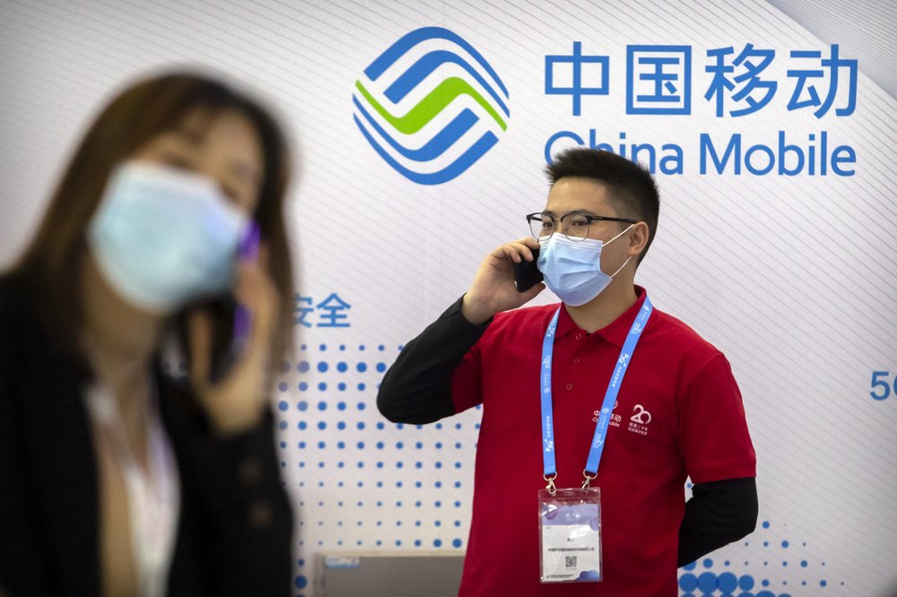 People wearing face masks to protect against the spread of the coronavirus talk on their cellphones near a booth for Chinese telecommunications firm China Mobile at the PT Expo in Beijing on Oct. 14, 2020. China said Saturday, Jan. 2, 2021, that it would take necessary countermeasures in response to the New York Stock Exchange's announcement that it would delist three major Chinese telecoms, in the latest flare-up of tensions between Beijing and Washington.