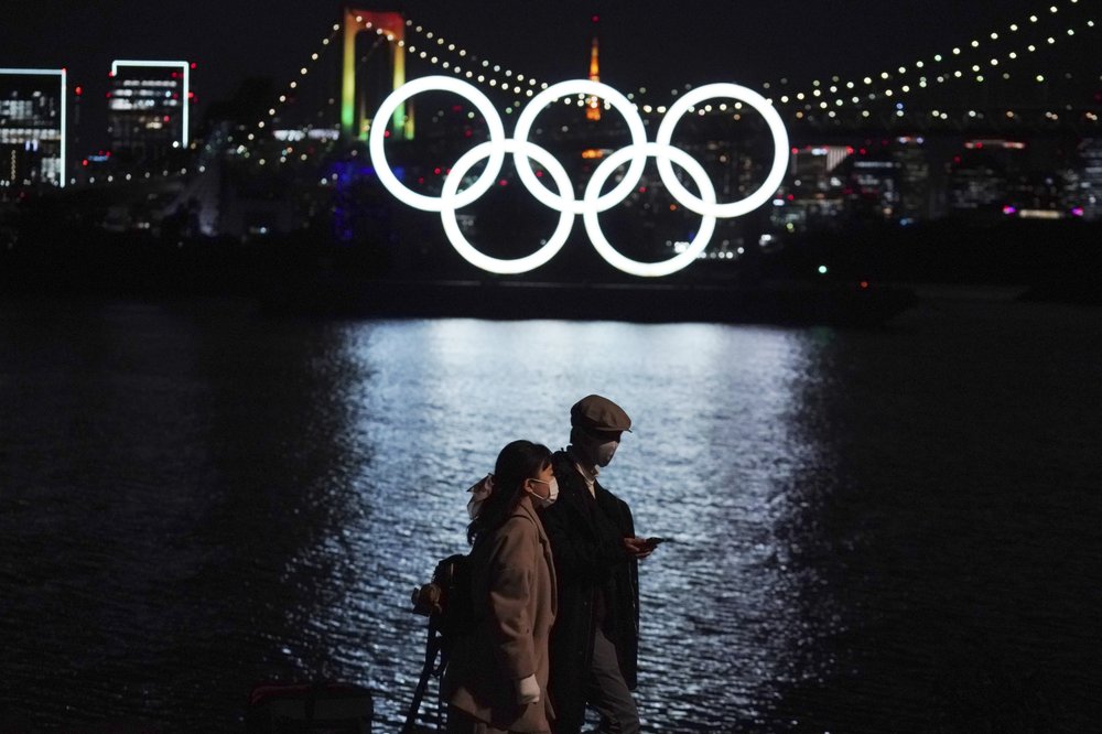 In this Dec. 1, 2020, file photo, a man and a woman walk past near the Olympic rings floating in the water in the Odaiba section in Tokyo. 