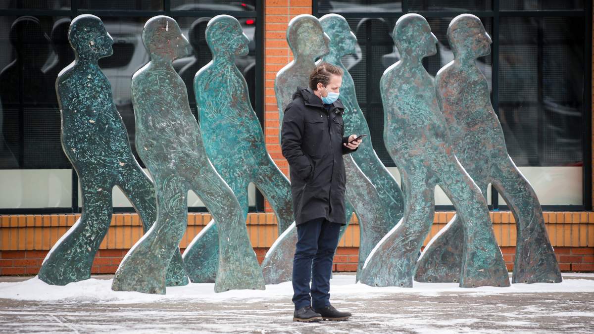 A pedestrian wearing a mask checks his mobile device while waiting to cross a street in Calgary, Alta., Thursday, Nov. 19, 2020, amid a worldwide COVID-19 pandemic. THE CANADIAN PRESS/Jeff McIntosh.