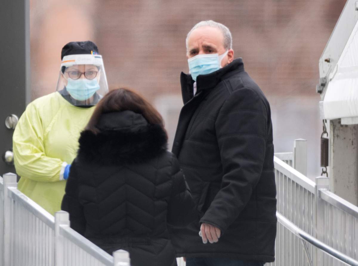 A health-care worker talks with people as they wait outside a COVID-19 testing clinic in Montreal, Sunday, January 3, 2021, as the COVID-19 pandemic continues in Canada and around the world. 