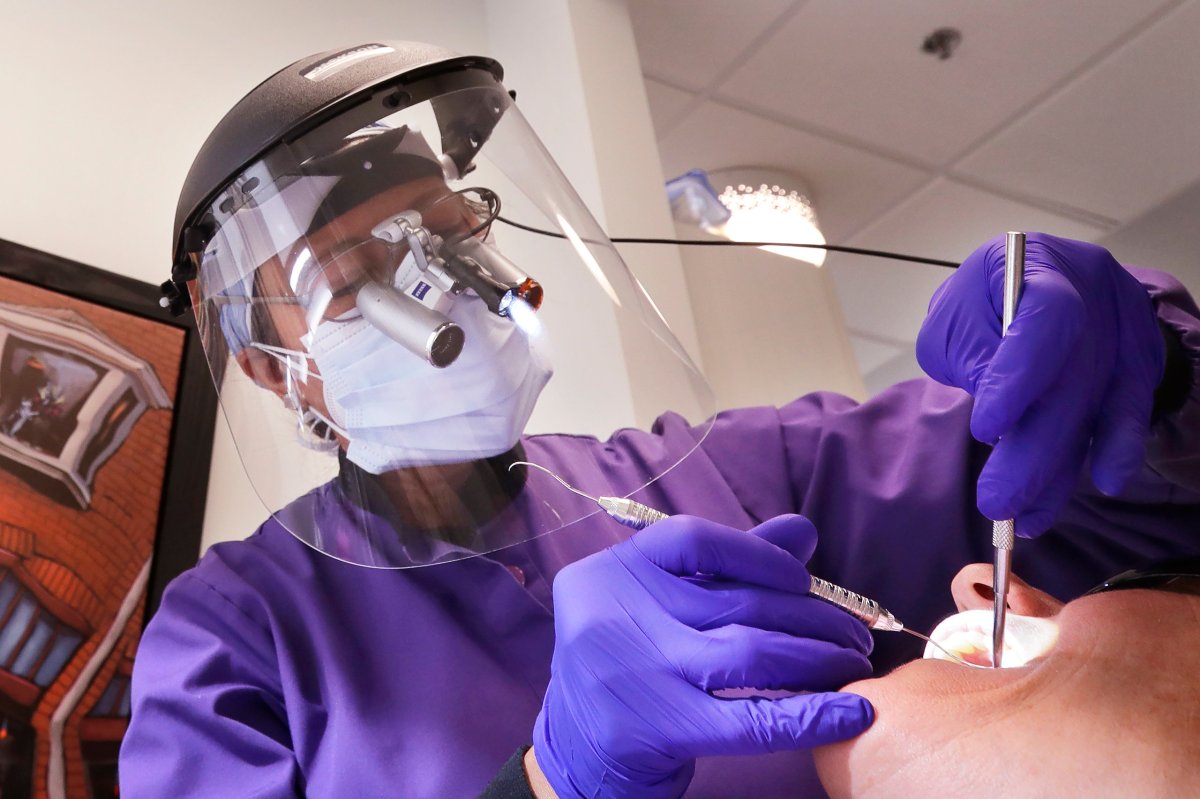 In this Wednesday, May 27, 2020 photo, dentist Dr. Kathleen Saturay wears additional protective equipment, including a face shield and disposable mask over a respirator mask, as she exams a patient in Seattle.  
