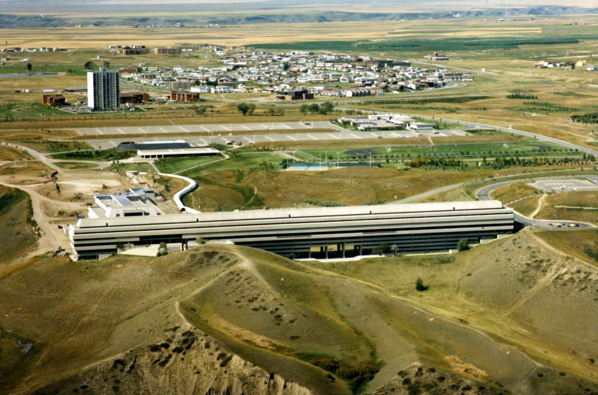 An aerial view of the University of Lethbridge, showing University Hall, the Performing Arts Wing, Physical Education building and support services buildings. Almost all of West Lethbridge is visible in the background. Taken in 1979.