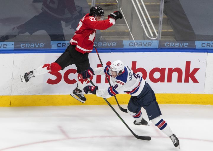 Canada’s Dylan Cozens (22) leaps as he is checked by United States’ Jake Sanderson (8) during second period IIHF World Junior Hockey Championship gold medal game action in Edmonton on Tuesday, January 5, 2021.