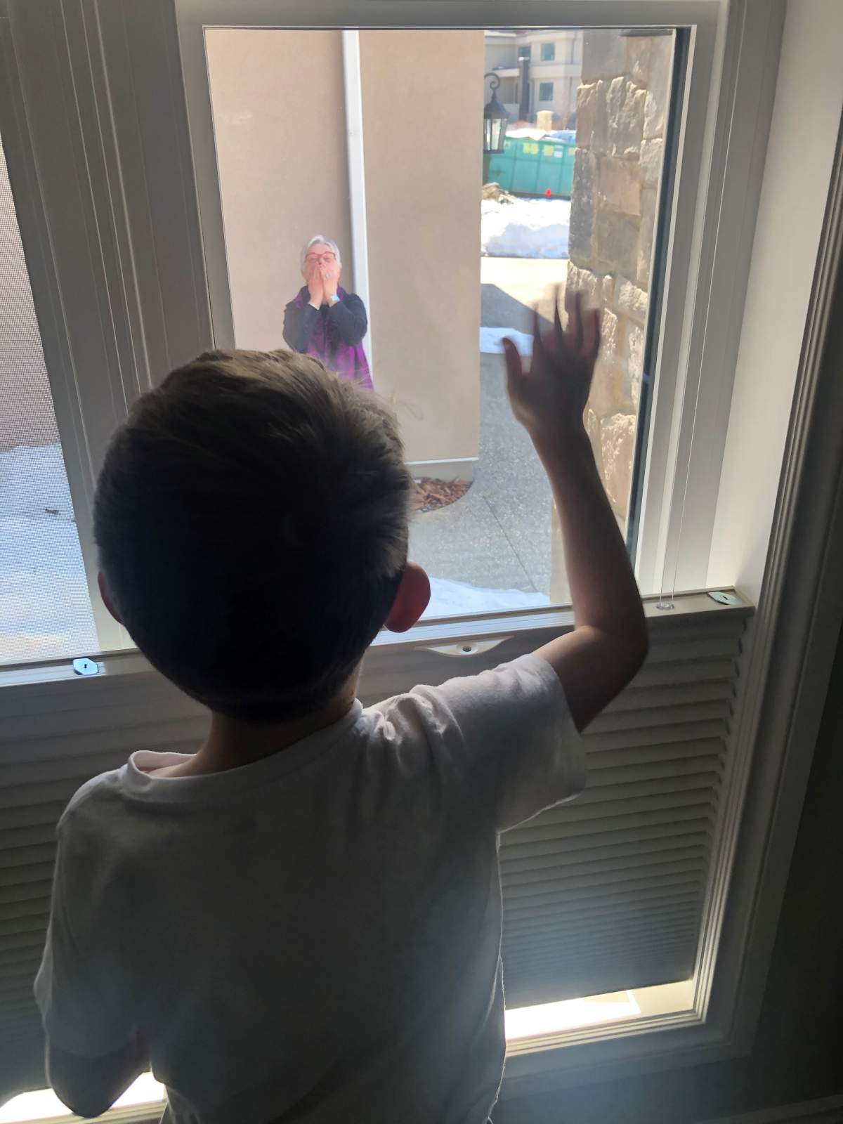 Caleb’s brother waves to his grandma from inside his home during a porch visit.