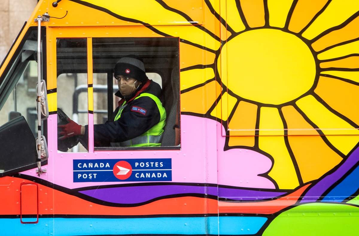A postal worker wears a mask to protect from COVID-19 while out delivering mail in Edmonton, Alta., on Thursday, Dec. 17, 2020.