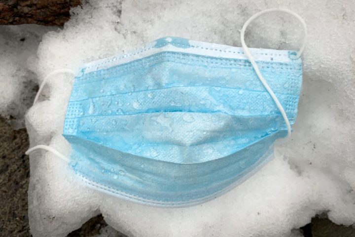 A discarded disposable mask is pictured on snow.
