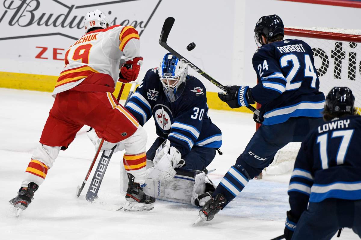 Winnipeg Jets goaltender Laurent Brossoit (30) makes a save on Calgary Flames’ Matthew Tkachuk (19) as Derek Forbort (24) defends during third period NHL action in Winnipeg on Tuesday, Feb. 2, 2021.