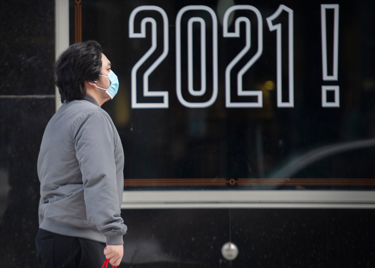 A man wears a face mask as he walks by a sign reading 2021! in Montreal, Saturday, February 6, 2021, as the COVID-19 pandemic continues in Canada and around the world.