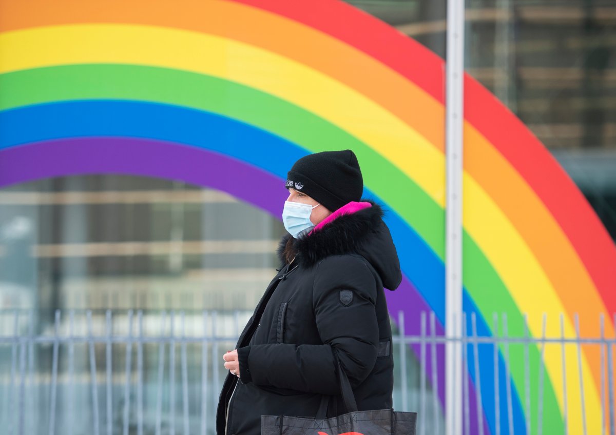A woman wears a face mask as she walks by a rainbow in Montreal, Saturday, February 6, 2021, as the COVID-19 pandemic continues in Canada and around the world. 
