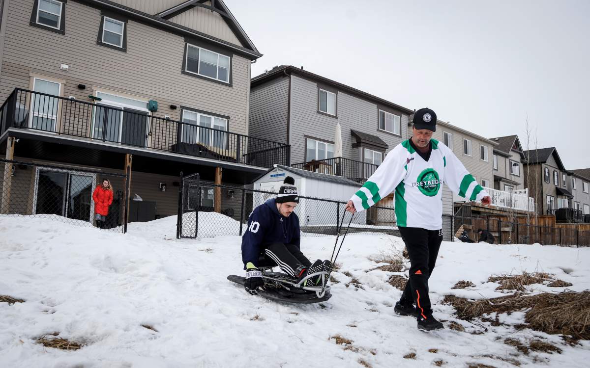 Tom Straschnitzki, right, helps his son, Humboldt Broncos bus crash survivor Ryan Straschnitzki, down a slope to a frozen pond to play pond hockey with his family near his home in Airdrie, Alta., Sunday, Jan. 31, 2021.