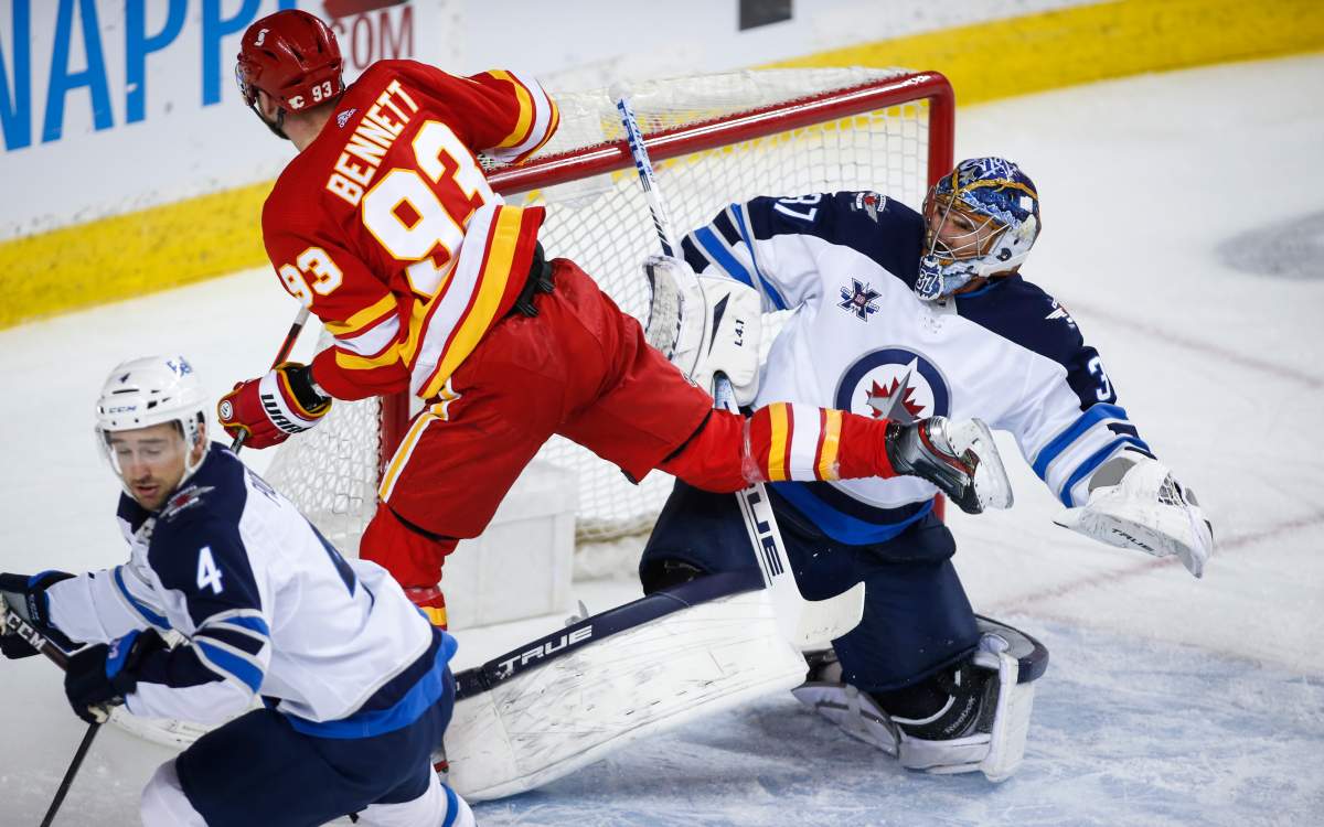 Winnipeg Jets goalie Connor Hellebuyck, right, reacts as Calgary Flames’ Sam Bennett crashes into him during first period NHL hockey action in Calgary, Tuesday, Feb. 9, 2021.