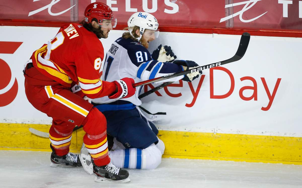 Winnipeg Jets’ Kyle Connor, right, is checked by Calgary Flames’ Chris Tanev during second period NHL hockey action in Calgary, Tuesday, Feb. 9, 2021.
