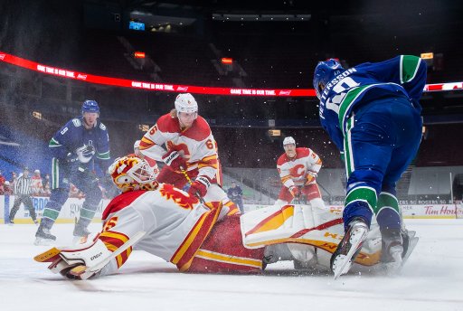 Vancouver Canucks’ Elias Pettersson, of Sweden, trips over Calgary Flames goalie Jacob Markstrom (25), of Sweden, during the third period of an NHL hockey game in Vancouver, on Saturday, Feb. 13, 2021.
