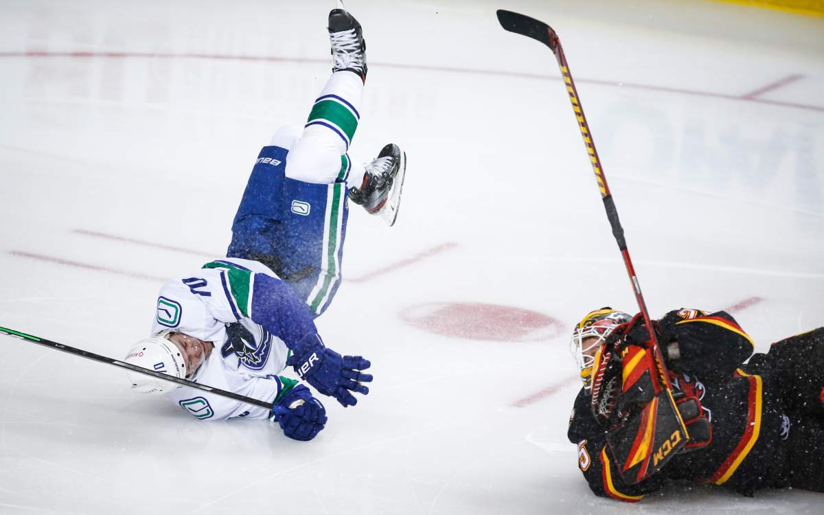 Vancouver Canucks’ Tanner Pearson, left, crashes over Calgary Flames goalie Jacob Markstrom during second period NHL hockey action in Calgary, Wednesday, Feb. 17, 2021.