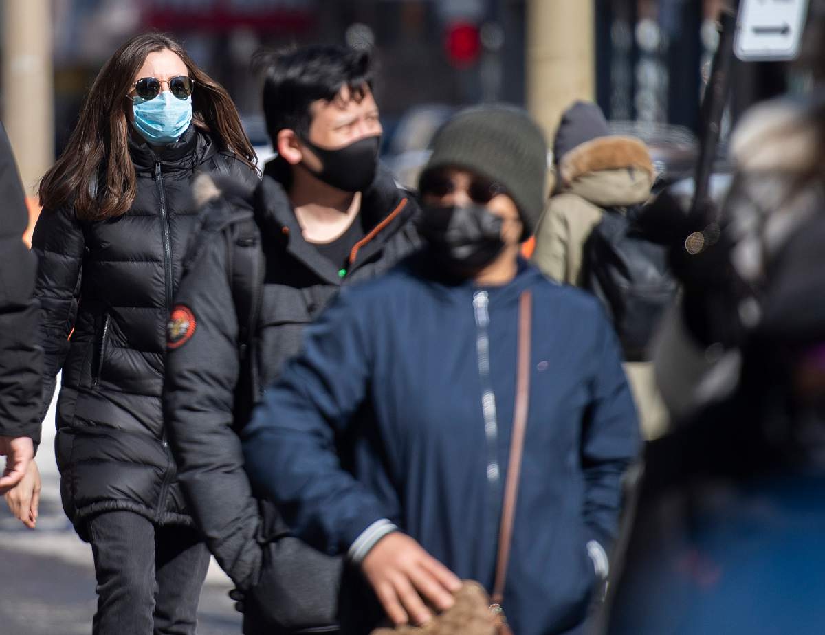 People wear face masks as they walk along a street in Montreal, Sunday, February 21, 2021, as the COVID-19 pandemic continues in Canada and around the world.