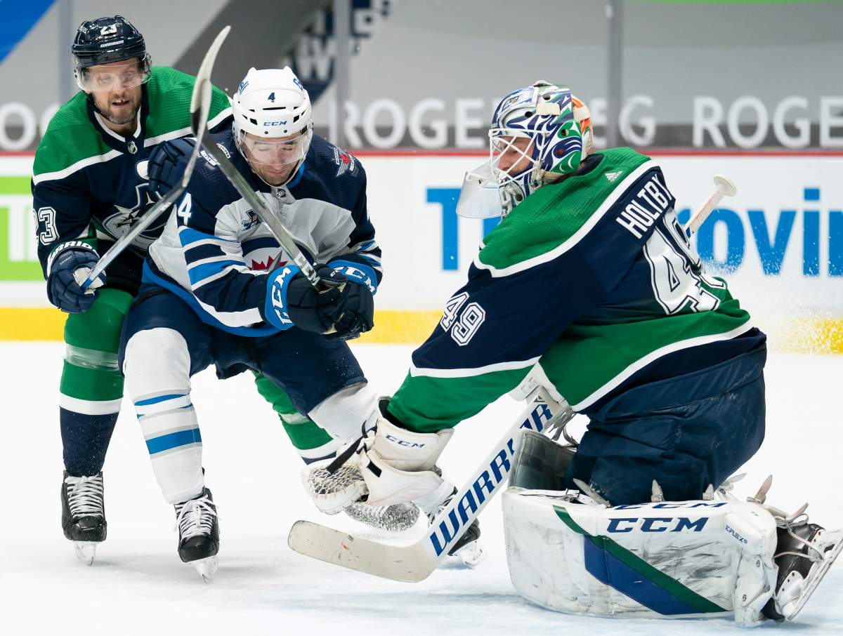 Vancouver Canucks goaltender Braden Holtby (49) stops a shot from Winnipeg Jets defenceman Neal Pionk (4) as Vancouver Canucks defenceman Alexander Edler (23) looks on during first-period NHL action in Vancouver, Sunday, Feb. 21, 2021.