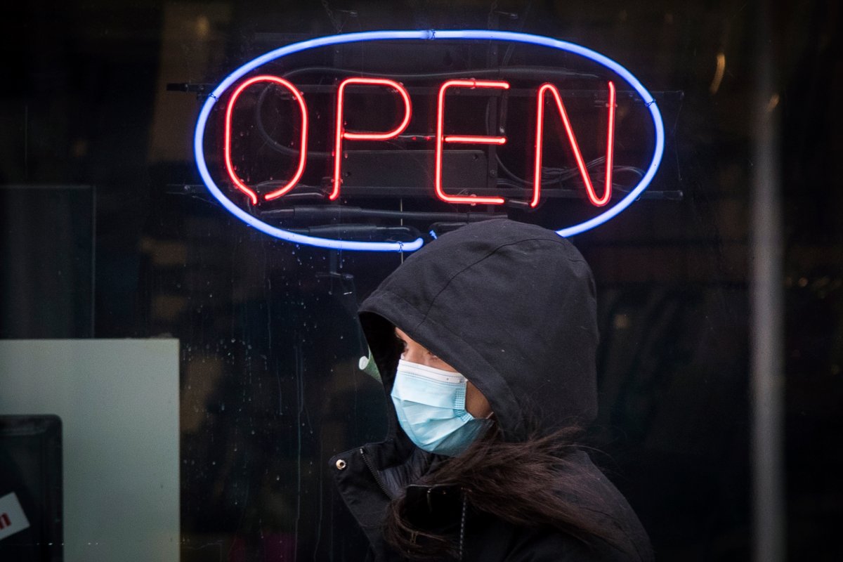 A person wears a mask to protect them from the COVID-19 virus while walking past an open sign in Kingston, Ontario on Thursday, February 11, 2021. 