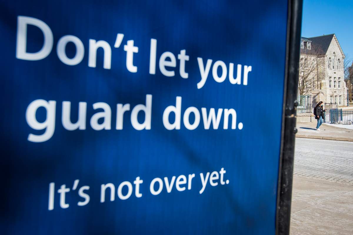 FILE - A person wears a disposable mask to protect them from the COVID-19 virus as they walk by a poster to follow public health guidelines, in Kingston, Ont., on Tuesday, March 2, 2021. 