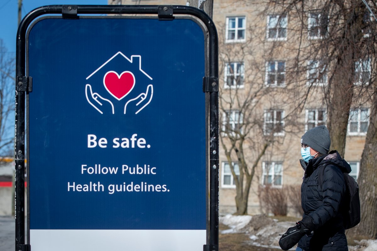 A person wears a mask to protect them from the COVID-19 virus, as they walk by a poster to follow public health guidelines, in Kingston March 2, 2021. 