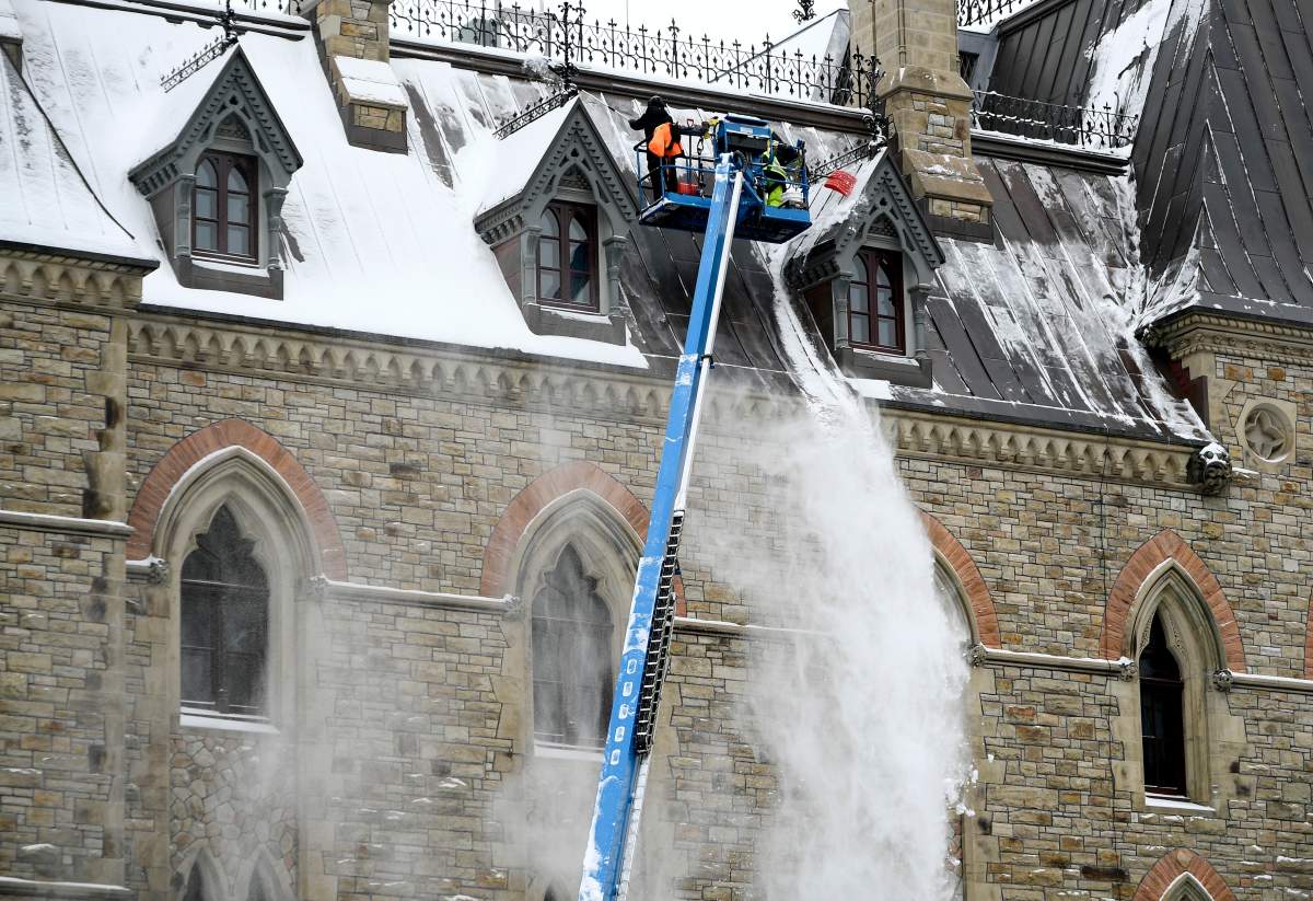 Workers on a boom lift use shovels to remove snow from the roof of Parliament Hill's West Block after an overnight snowfall in Ottawa earlier this winter. The region is due for another blast of snow on March 1, 2021.