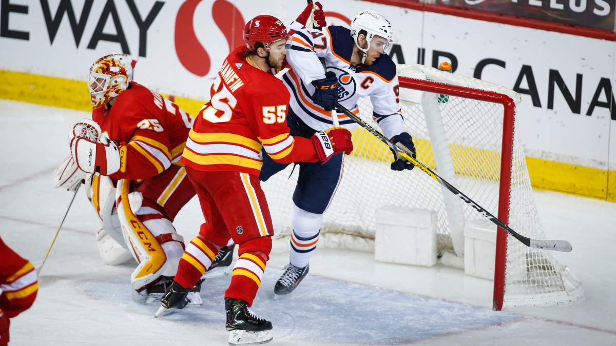Edmonton Oilers’ Connor McDavid, right, is checked by Calgary Flames’ Andrew Mangiapane, centre, as goalie Jacob Markstrom guards the net during third-period NHL hockey action in Calgary on Monday, March 15, 2021.