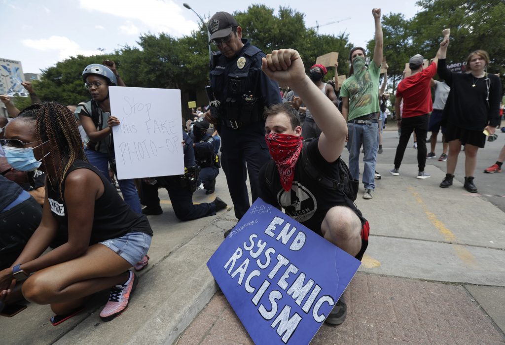 A demonstrator protests members of the Austin Police Department kneeling with other demonstrators who gathered in Austin, Texas, Saturday, June 6, 2020, to protest the death of George Floyd, a black man who was in police custody in Minneapolis. Floyd died after being restrained by Minneapolis police officers on Memorial Day. (AP Photo/Eric Gay).