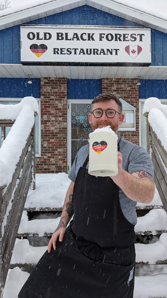 Nathan Guggenheimer holds up a beer in front of the Old Black Forest Restaurant.