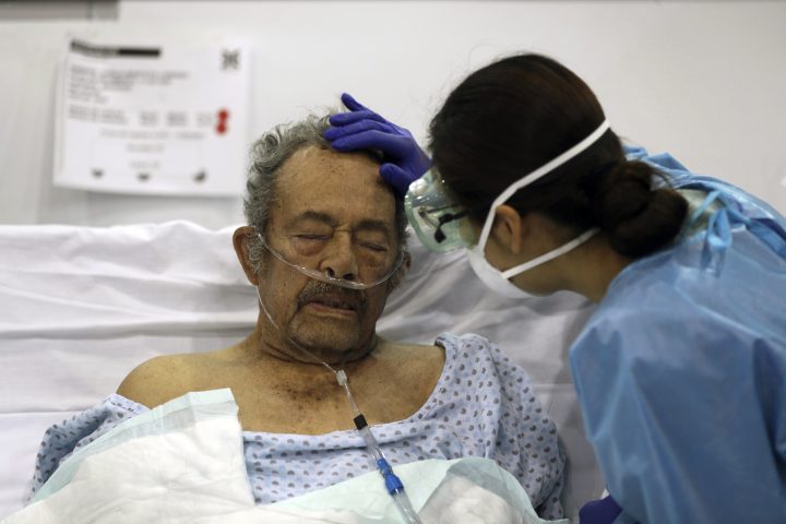 FILE - In this March 11, 2021 file photo, a healthcare worker strokes the forehead of a COVID-19 patient in a field hospital set up inside the Citibanamex convention center in Mexico City, on the first year anniversary that the World Health Organization declared the coronavirus a pandemic. As Mexico approaches 200,000 in officially test-confirmed deaths from COVID-19, the real death toll is probably higher due to the country’s extremely low rate of testing. (AP Photo/Fernando Llano, File).