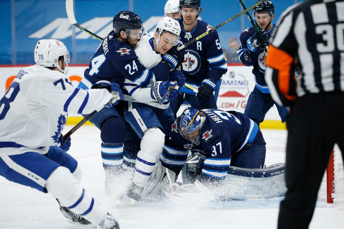 Winnipeg Jets' Derek Forbort (24) wraps up Toronto Maple Leafs' Zach Hyman (11) as his goaltender Connor Hellebuyck (37) covers the puck during first period NHL action in Winnipeg on Friday, April 2, 2021.