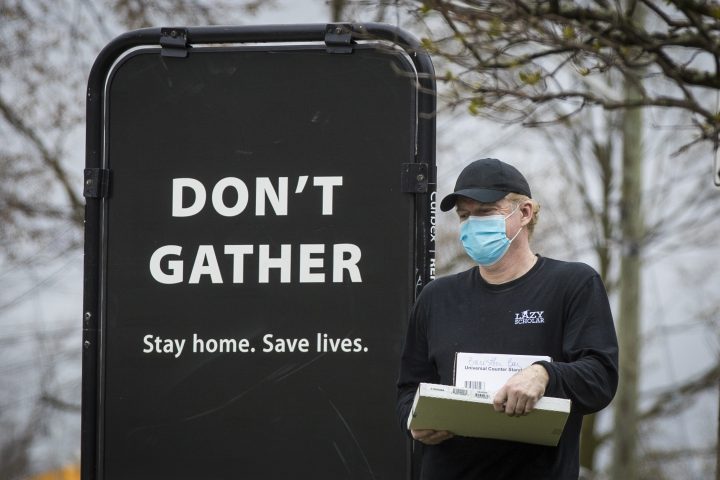 A person wears a surgical mask to protect them from COVID-19 while walking by a sign advising not to gather during the ongoing pandemic in Kingston on Friday, April 16, 2021.