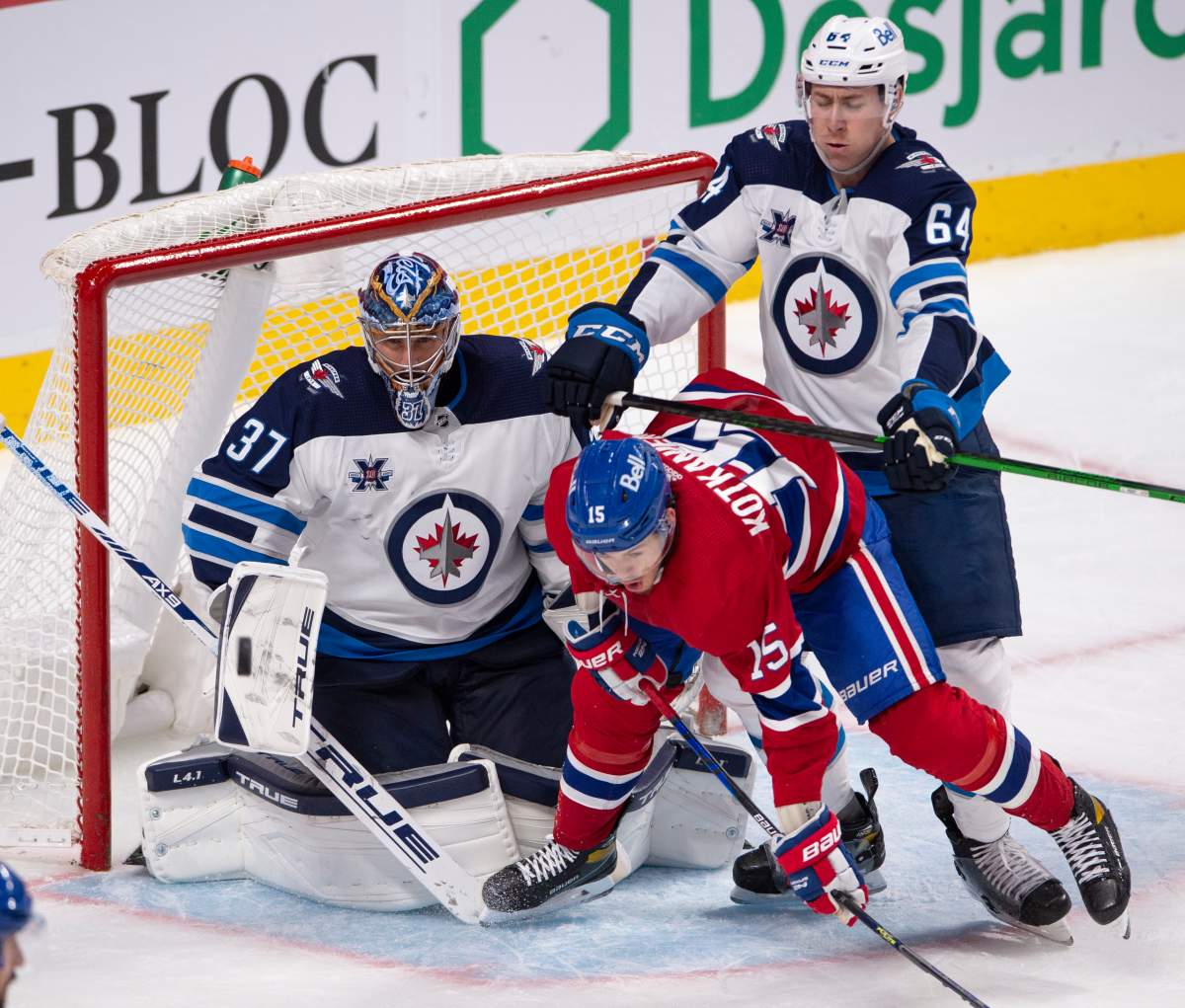 Winnipeg Jets' Logan Stanley (64) crosschecks Montreal Canadiens' Jesperi Kotkaniemi (15) in front of Jets goaltender Connor Hellebuyck (37) during third period NHL hockey action Thursday, April 8, 2021 in Montreal. 