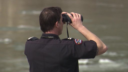 An Edmonton firefighter searching the North Saskatchewan River with binoculars in Edmonton, Alta. on Tuesday, April 6, 2021.
