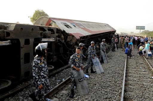 Security forces stand guard as people gather at the site where a passenger train derailed in Egypt, Sunday, April 18, 2021. At least eight train wagons ran off the railway, the provincial governor’s office said in a statement. (AP Photo/Tarek Wagih)