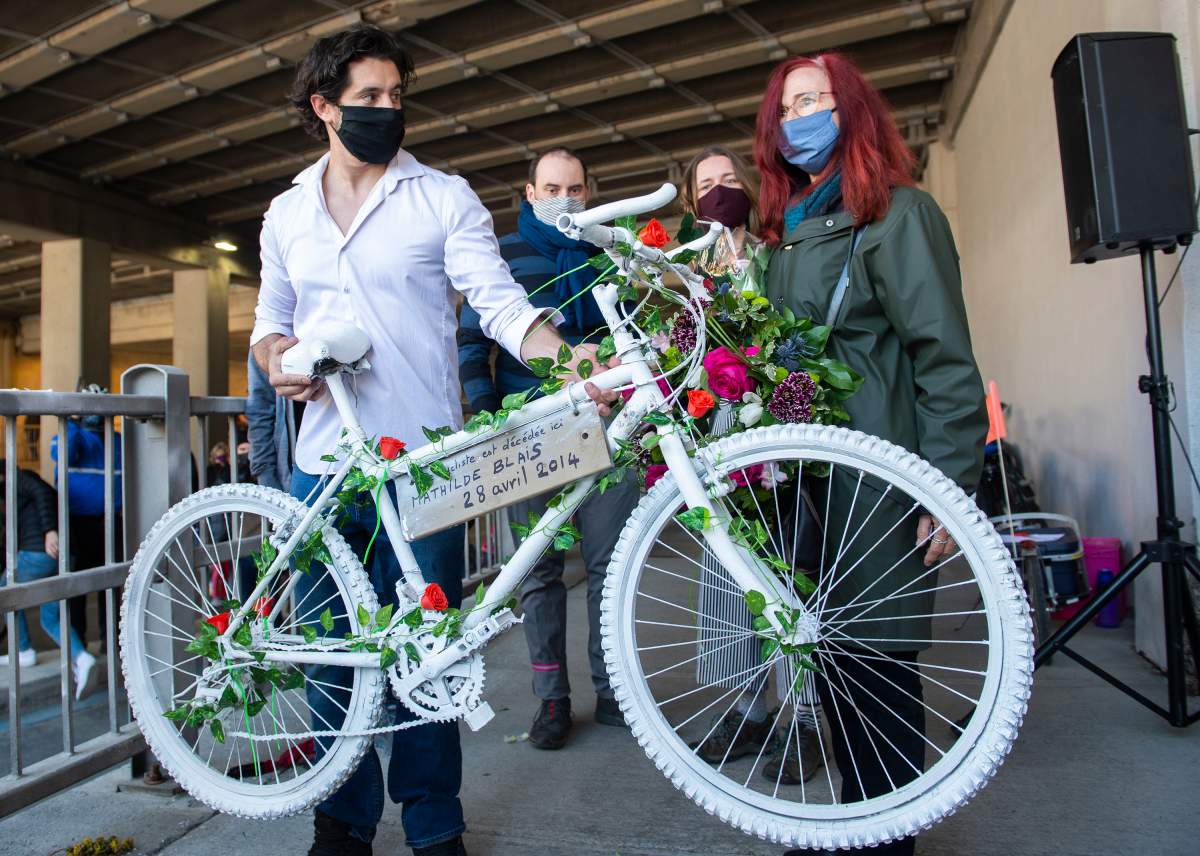 Karim Kammah, left, of Velo Fantome, hands a white bicycle to Genevieve Laborde, mother of Mathilde Blais, during a ceremony in Montreal, Sunday, May 2, 2021. Blais was killed at this spot in 2014 and the bike has been donated to the Museum of Civilization in Quebec City.