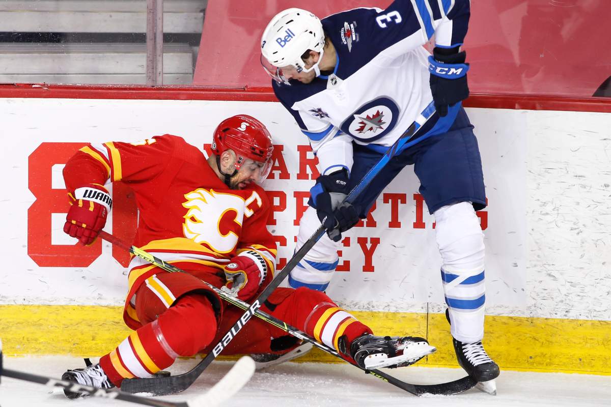 Winnipeg Jets’ Tucker Poolman, right, digs for the puck under Calgary Flames’ Mark Giordano during first period NHL hockey action in Calgary on Wednesday, May 5, 2021.
