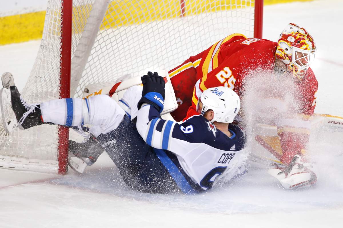 Winnipeg Jets’ Andrew Copp, left, slides into Calgary Flames goalie Jacob Markstrom, from Sweden, during third period NHL hockey action in Calgary on Wednesday, May 5, 2021.
