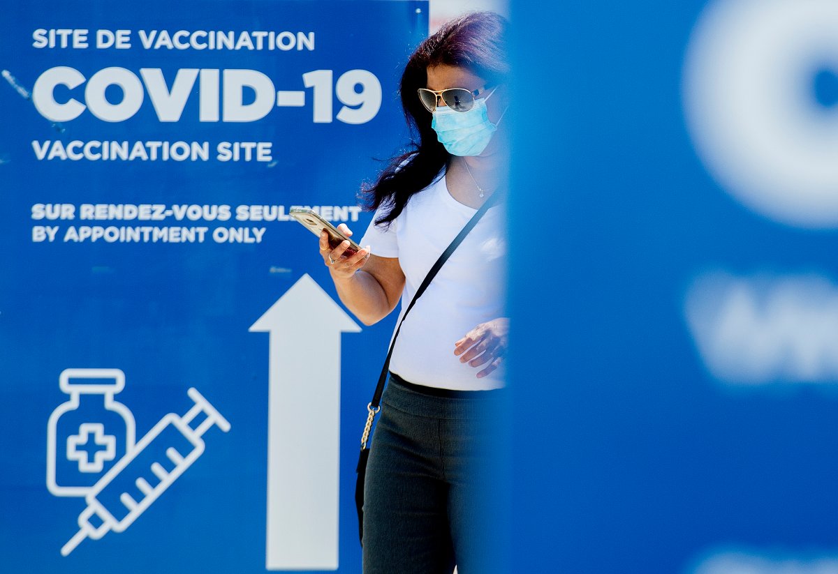 A woman wears a face mask as she walks by a sign for a COVID-19 vaccination site in Montreal, Sunday, May 16, 2021, as the COVID-19 pandemic continues in Canada and around the world. THE CANADIAN PRESS/Graham Hughes.