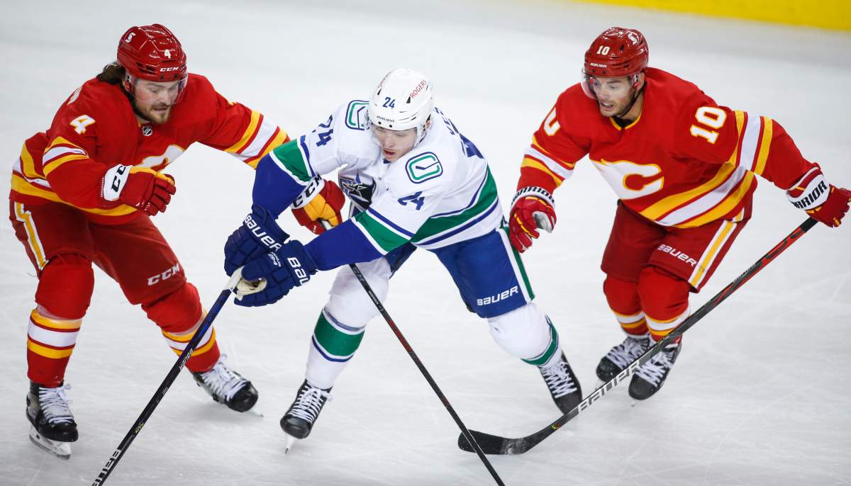 Vancouver Canucks’ Jimmy Vesey, centre, is checked by Calgary Flames’ Rasmus Andersson, left, and Derek Ryan during second period NHL hockey action in Calgary, Wednesday, May 19, 2021.