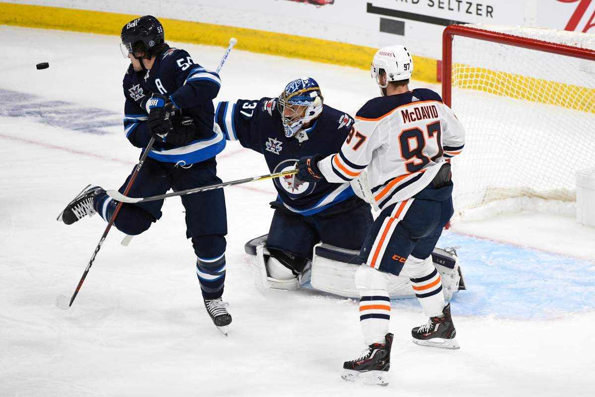 A shot by the Edmonton Oilers goes wide of net past Winnipeg Jets’ Mark Scheifele (55) and goaltender Connor Hellebuyck (37) as Connor McDavid (97) looks for the deflection during first period NHL Stanley Cup playoff action in Winnipeg on Sunday, May 23, 2021.