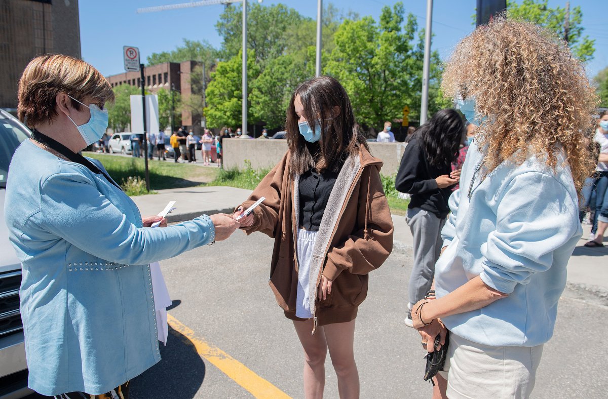 Lucie Tremblay of the Montreal Centre-West Health Service, left, hands a coupon for a time to receive a COVID-19 vaccine to Victoria Dumont (14) as her mother Myriam Achard looks on at the Bill-Durnan COVID-19 vaccination site in Montreal, Monday, May 24, 2021, as the COVID-19 pandemic continues in Canada and around the world. 