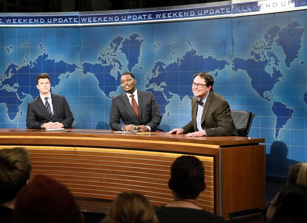 This image released by NBC shows, from left, Colin Jost, Michael Che, and host Elon Musk as financial expert Lloyd Ostertag during the "Weekend Update" sketch on "Saturday Night Live," in New York on May 8, 2021. (Will Heath/NBC via AP).
