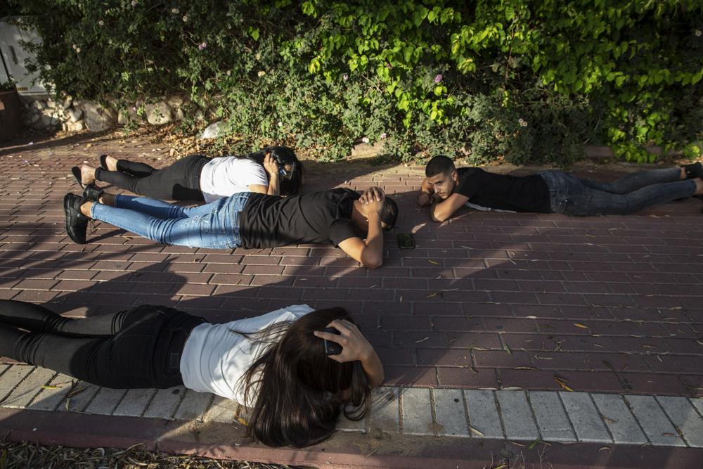 Israelis take cover as a siren sounds a warning of incoming rockets fired from the Gaza Strip, in Ashkelon, southern Israel, Sunday, May 16, 2021. (AP Photo/Heidi Levine)