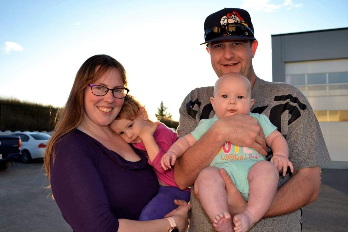 Kira Arneson holding her daughter Lyllian Koncz with partner Cody Koncz holding their daughter Emma Koncz | Photo credit: All The Things Photography
