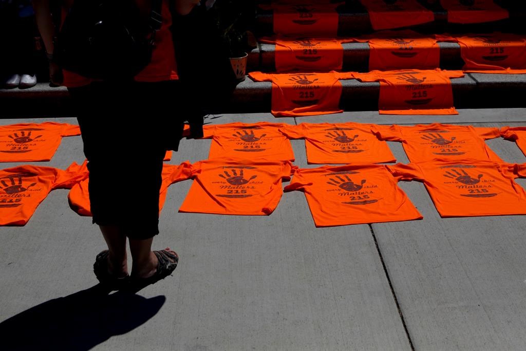 A woman looks over orange shirts, shoes, flowers and messages displayed on the steps outside the legislature in Victoria on Tuesday, June 8, 2021 following a ceremony in honour of the 215 residential school children whose remains were detected near a former residential school at Kamloops, B.C. The Lower Kootenay Band in B.C.'s southern Interior says a search using ground-penetrating radar has also found the remains of 182 people in unmarked graves at another residential school site.THE CANADIAN PRESS/Chad Hipolito.